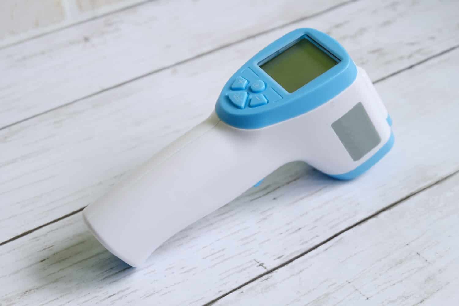Non-contact infrared thermometer on white wooden background to measure a body temperature. Healthcare and medical theme.