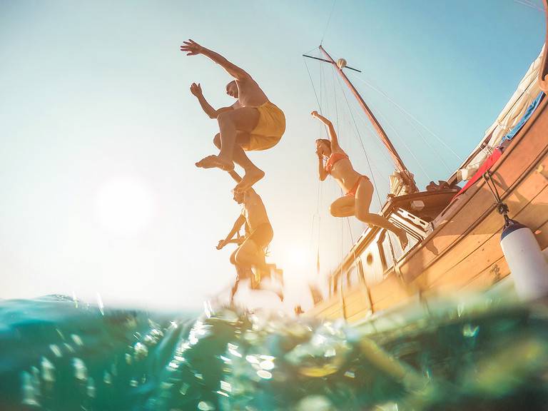 Happy friends diving from sailing boat into the sea - Young people jumping inside ocean in summer excursion day - Vacation, youth and fun concept - Main focus on close-up man - Fisheye lens distortion
