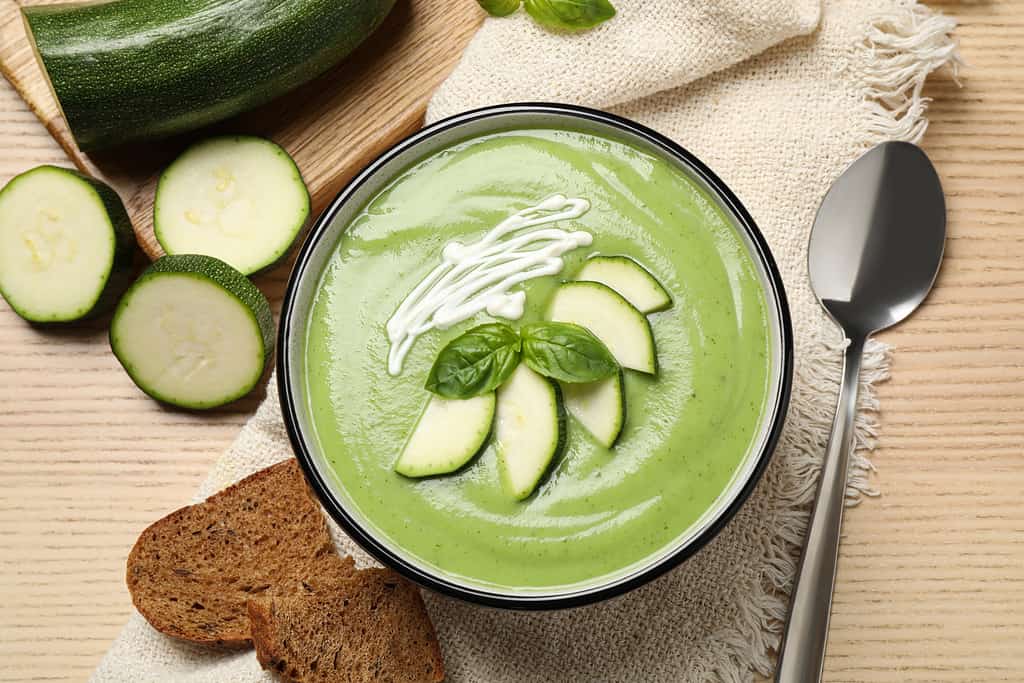 Tasty homemade zucchini cream soup served on wooden table, flat lay