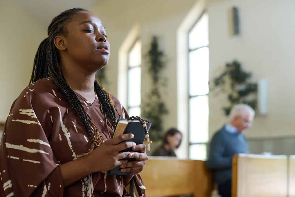 Young black woman in casual dress keeping her eyes closed during prayer