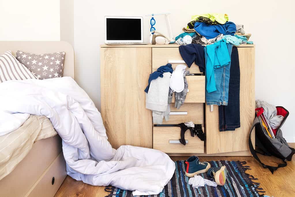 mess in a teenager's room. Clothes are strewn across the chest of drawers, floor