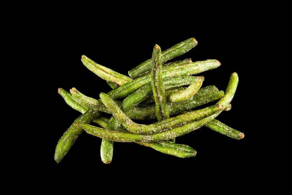 Natural chips of green string beans on black background, close-up. Crispy, dried vegetables with addition of molasses. Healthy vegan snack. Selective focus