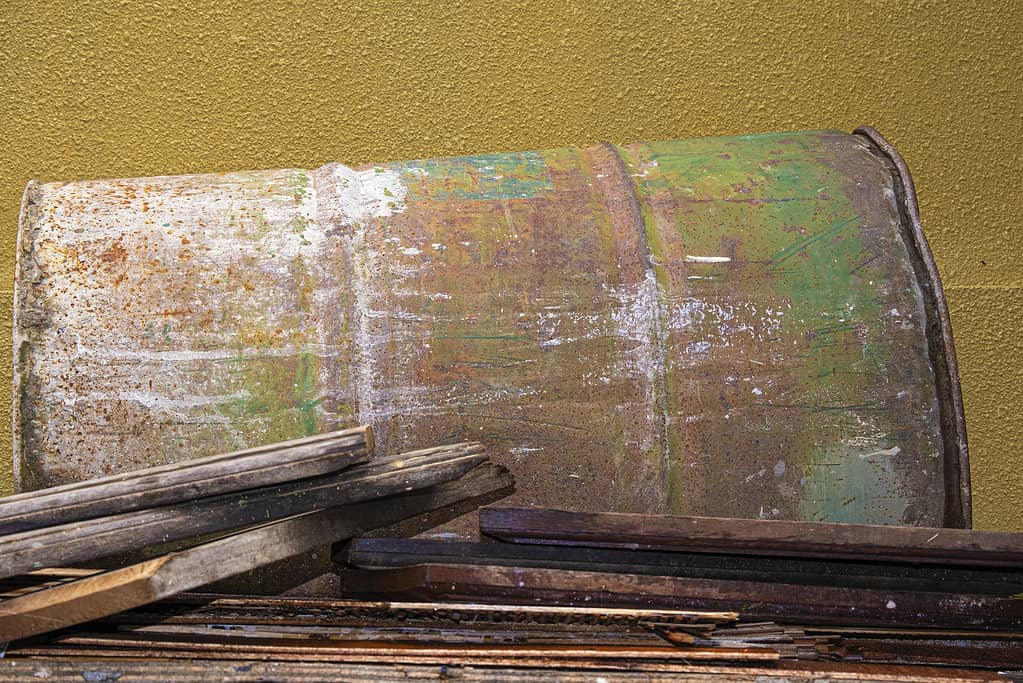 Rusted oil barrel laying on pile of wood planks