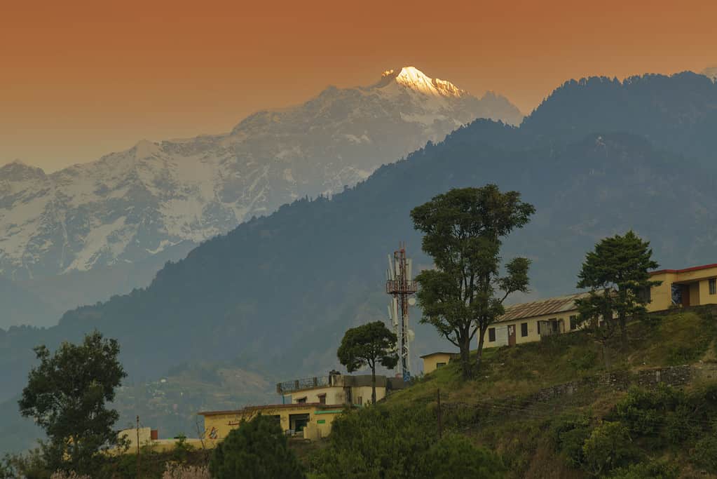 Snow capped mountain peak of Choukhamba range with tourist bungalows and resorts at Deoriatal, Uttarakhand, India. Sun set light on peak of famous Garhwal Himalayan mountain range.