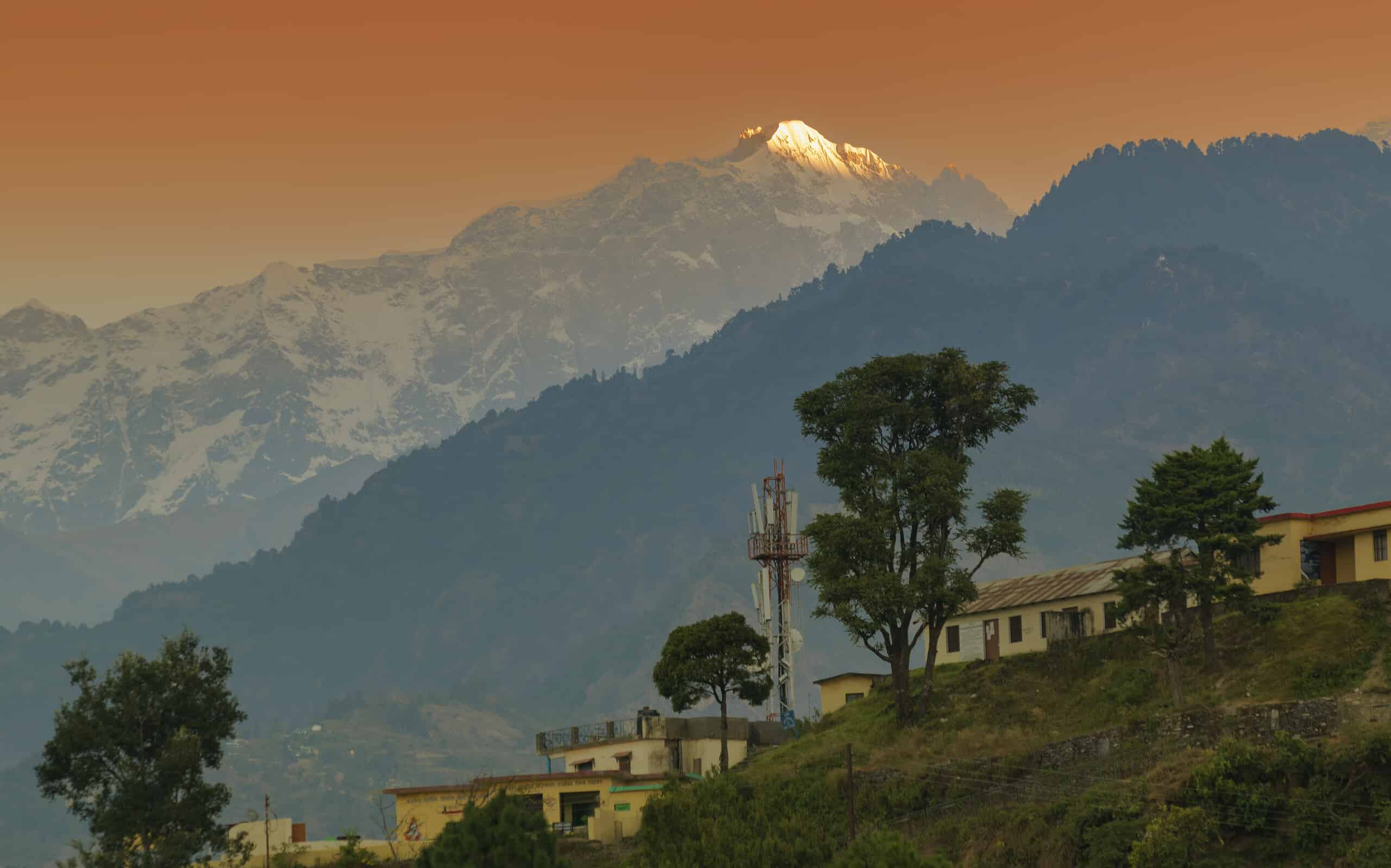 Snow capped mountain peak of Choukhamba range with tourist bungalows and resorts at Deoriatal, Uttarakhand, India. Sun set light on peak of famous Garhwal Himalayan mountain range.