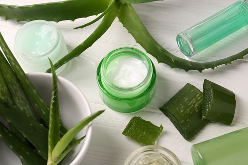 Different cosmetic products and cut aloe vera leaves on white wooden table, above view