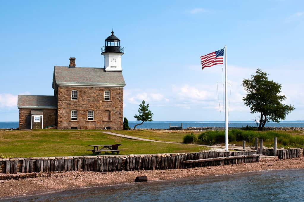 American flag flying near the stone beacon of Sheffield Island lighthouse in Connecticut on a warm sunny day. It is a popular summertime attraction.