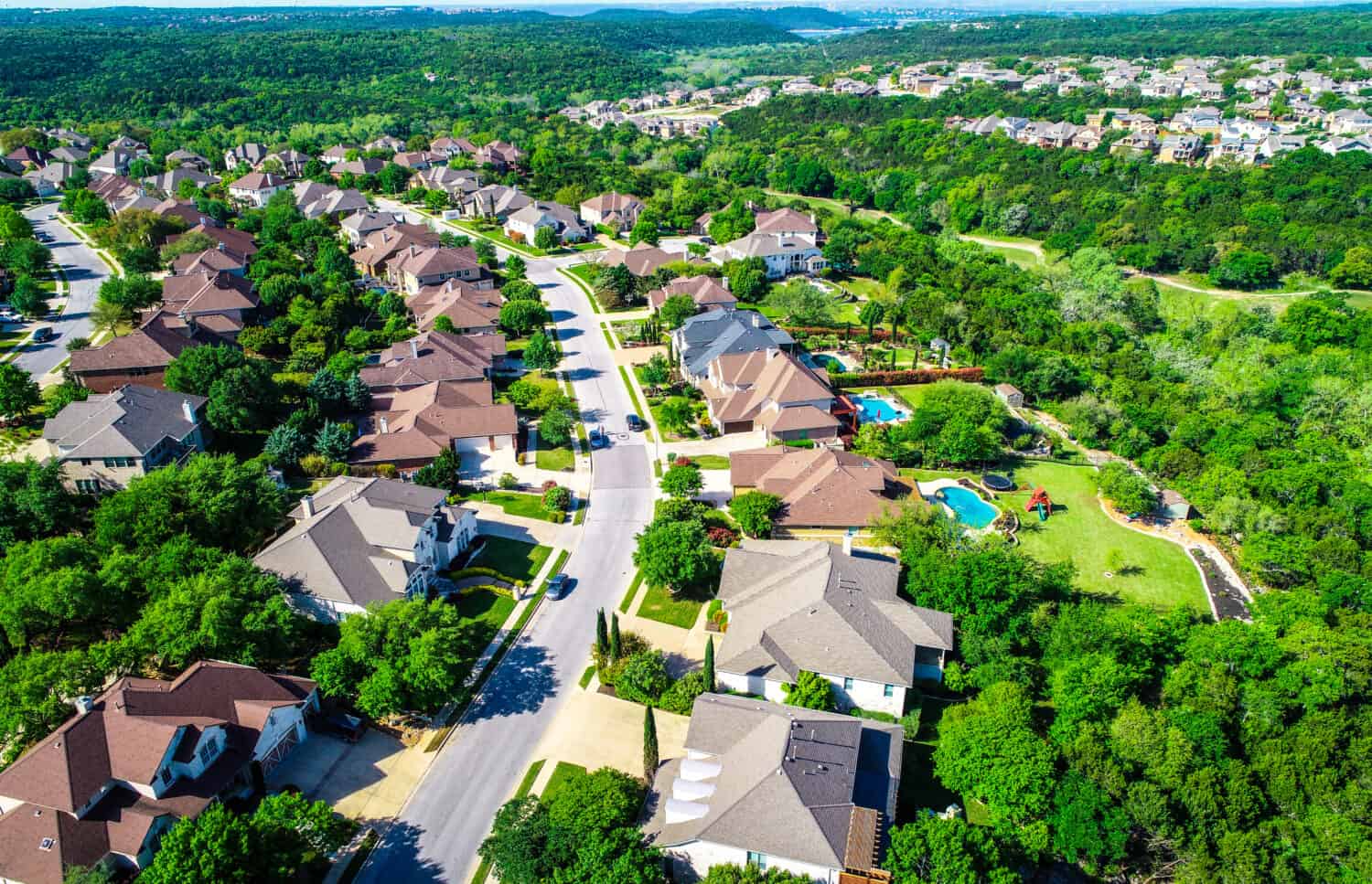 Aerial drone view above Curved road with mansion luxury homes leading into the hills green landscape Cedar Park Texas Suburb