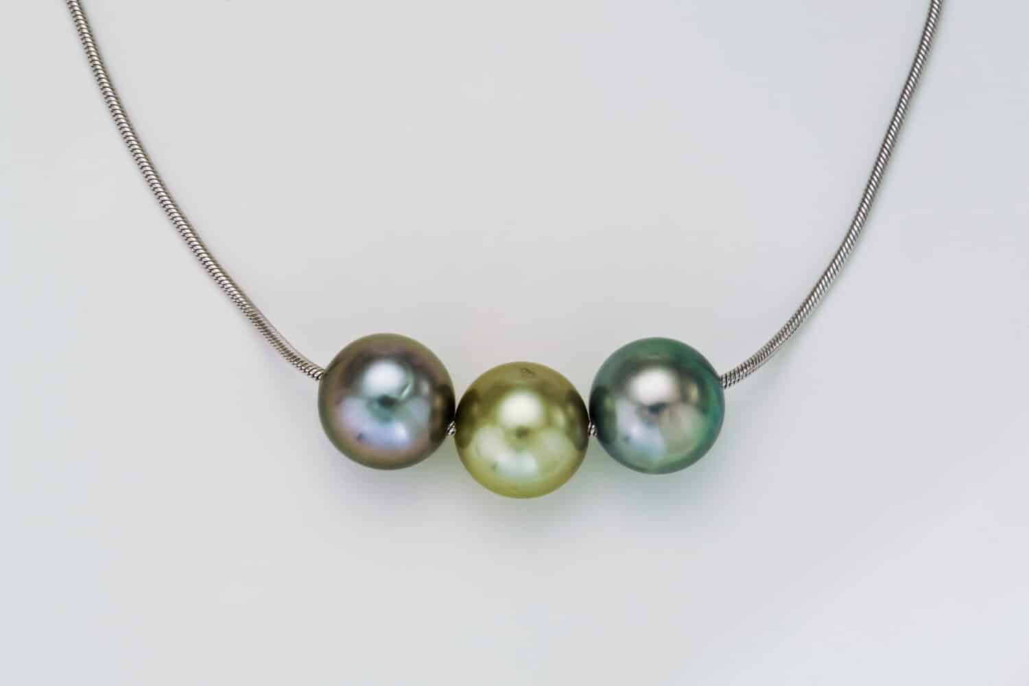 Three different light colored round Tahitian Pearls are shown on a white gold round neck chain. Shown on a white background.