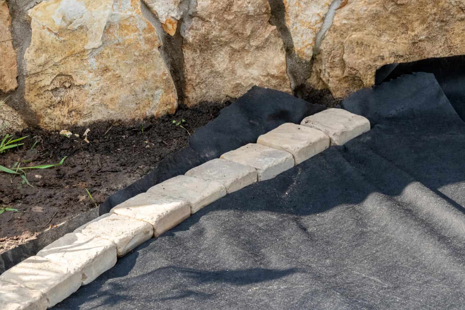 Edging of laid woven geotextile fabric with sandstone pavers in the summer garden under reconstruction