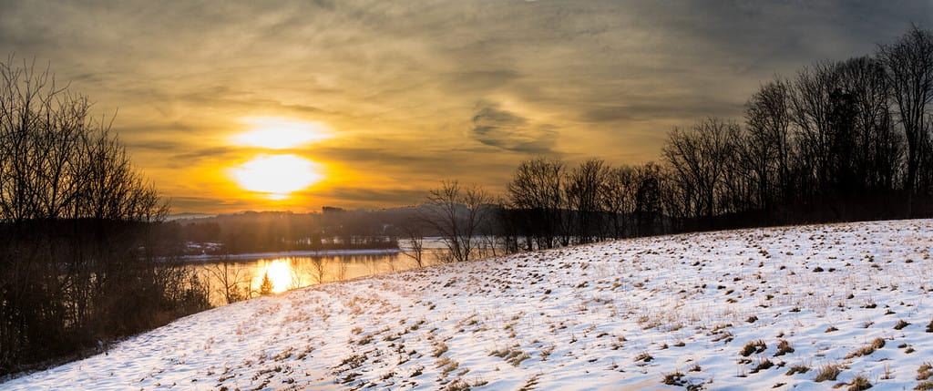 Panoramic landscape of Blue Marsh Lake in Berks County, PA in winter with a snow-covered field in the foreground