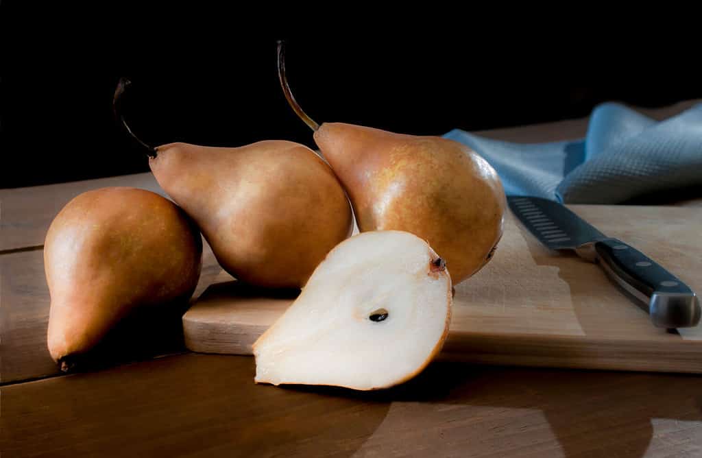 Bosc pears or brown pears on a cutting board with a knife on the side and a blue napkin at the back in a black background. Rim light or backlight