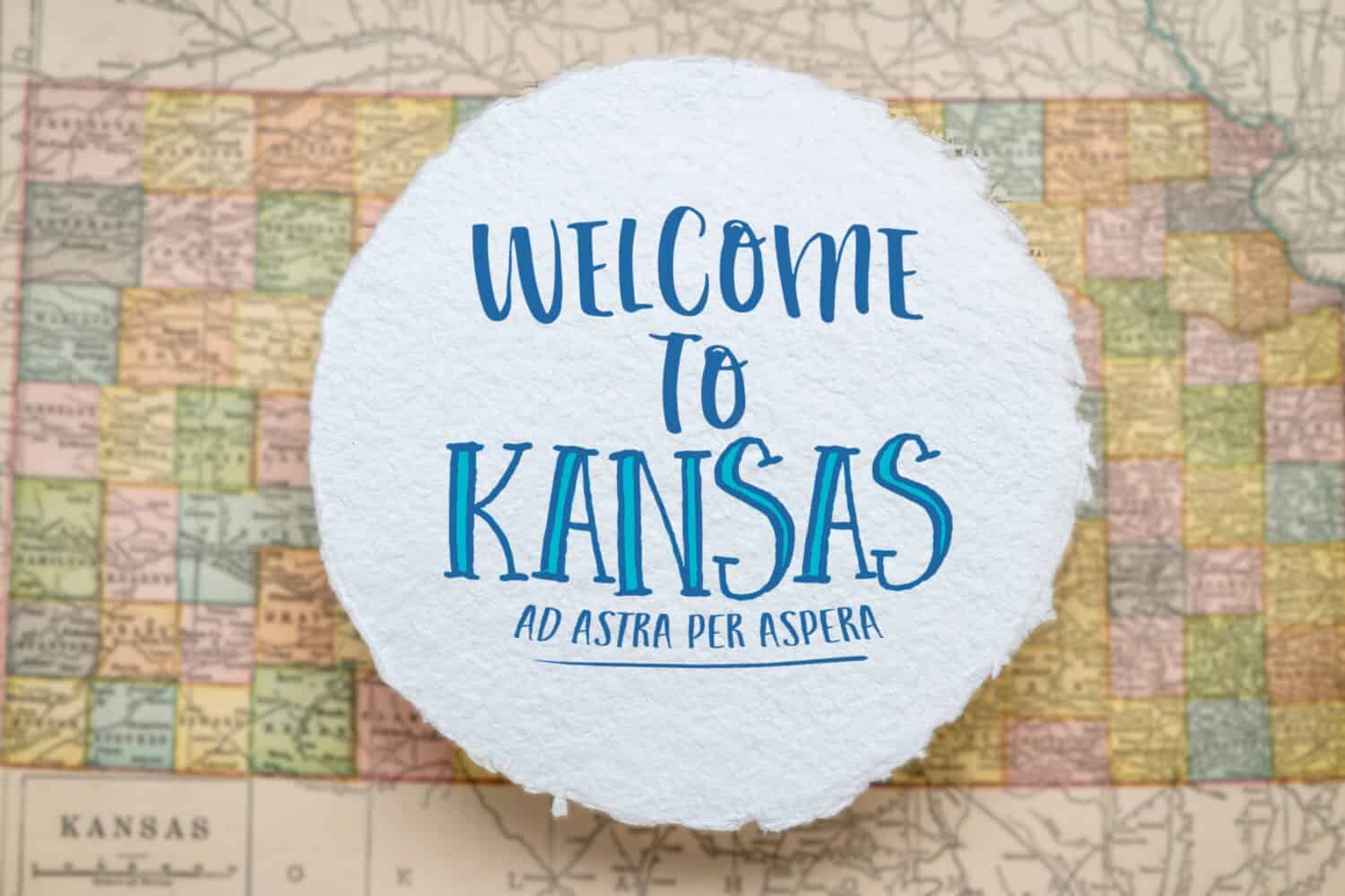 welcome to Kansas, ad astra per aspera (to the stars through hardships) - handwriting on a sheet of rough handmade paper floating over vintage defocused map of Kansas, hospitality and travel concept