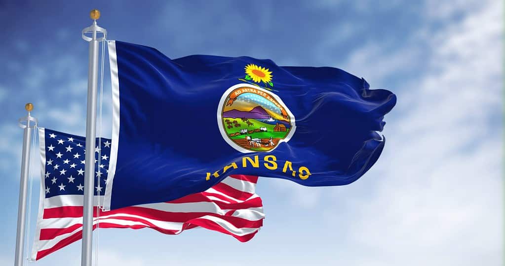 The Kansas state flag waving along with the national flag of the United States of America. In the background there is a clear sky. Kansas is a state in the Midwestern United States