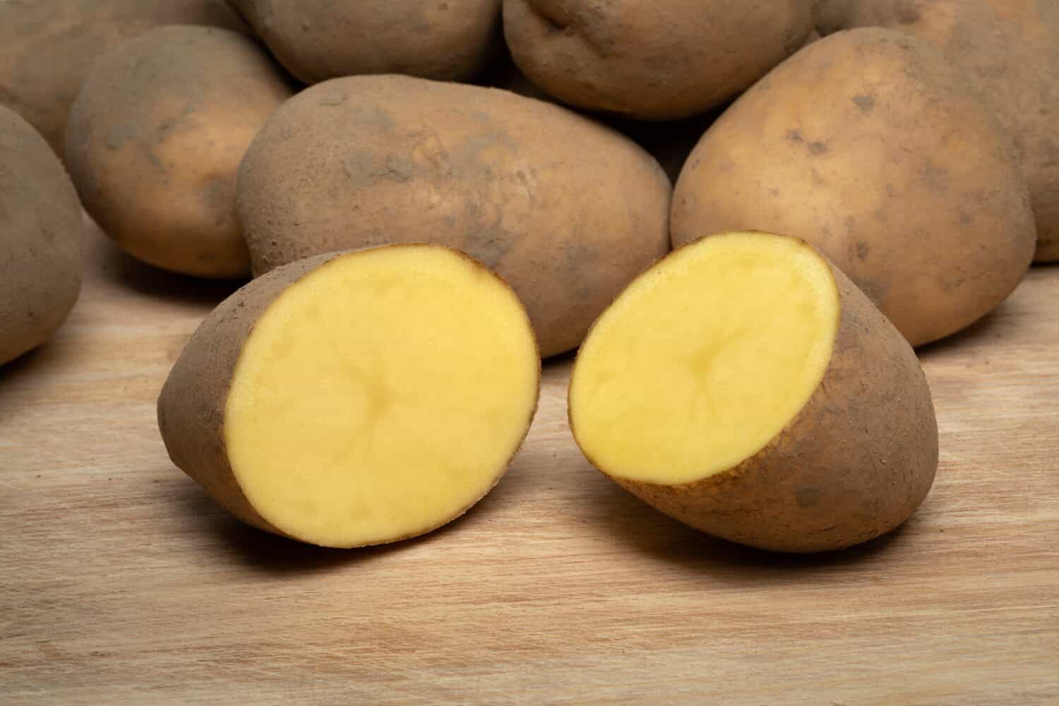 Dutch variety potato called Bintje whole and halved on wooden background close up 