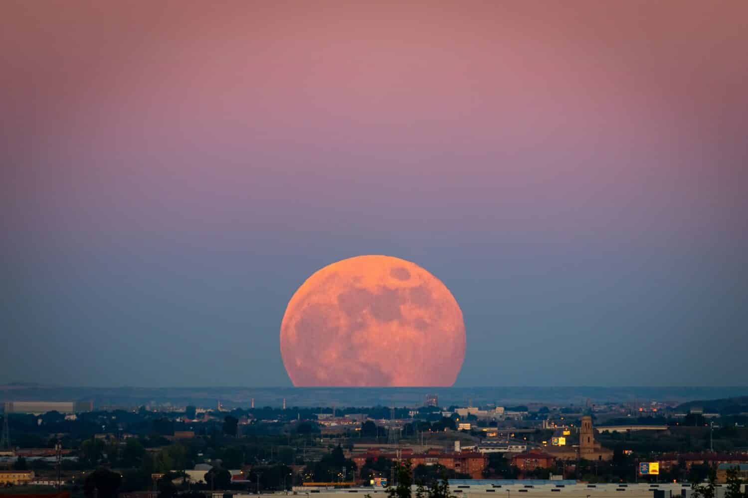 The strawberry Supermoon (Supermoon of strawberry) at sunset gradient from blue to pink on the city skyline in June 2020 in Spain.