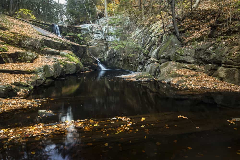 Blurred, misty water of a waterfall at Enders State Park in Granby, Connecticut, with reflections of the falls and autumn leaves in the dark water.
