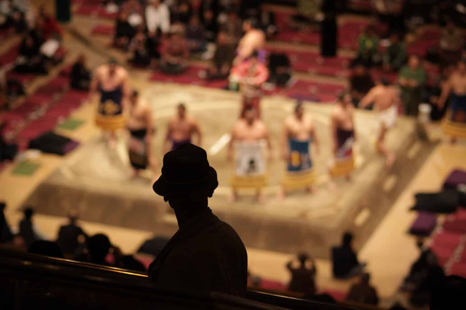 Silhouette of an elderly man watching sumo wrestlers standing in a ceremonial ring