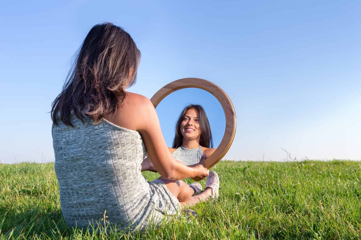 Woman sitting on grass looking at  her mirror image