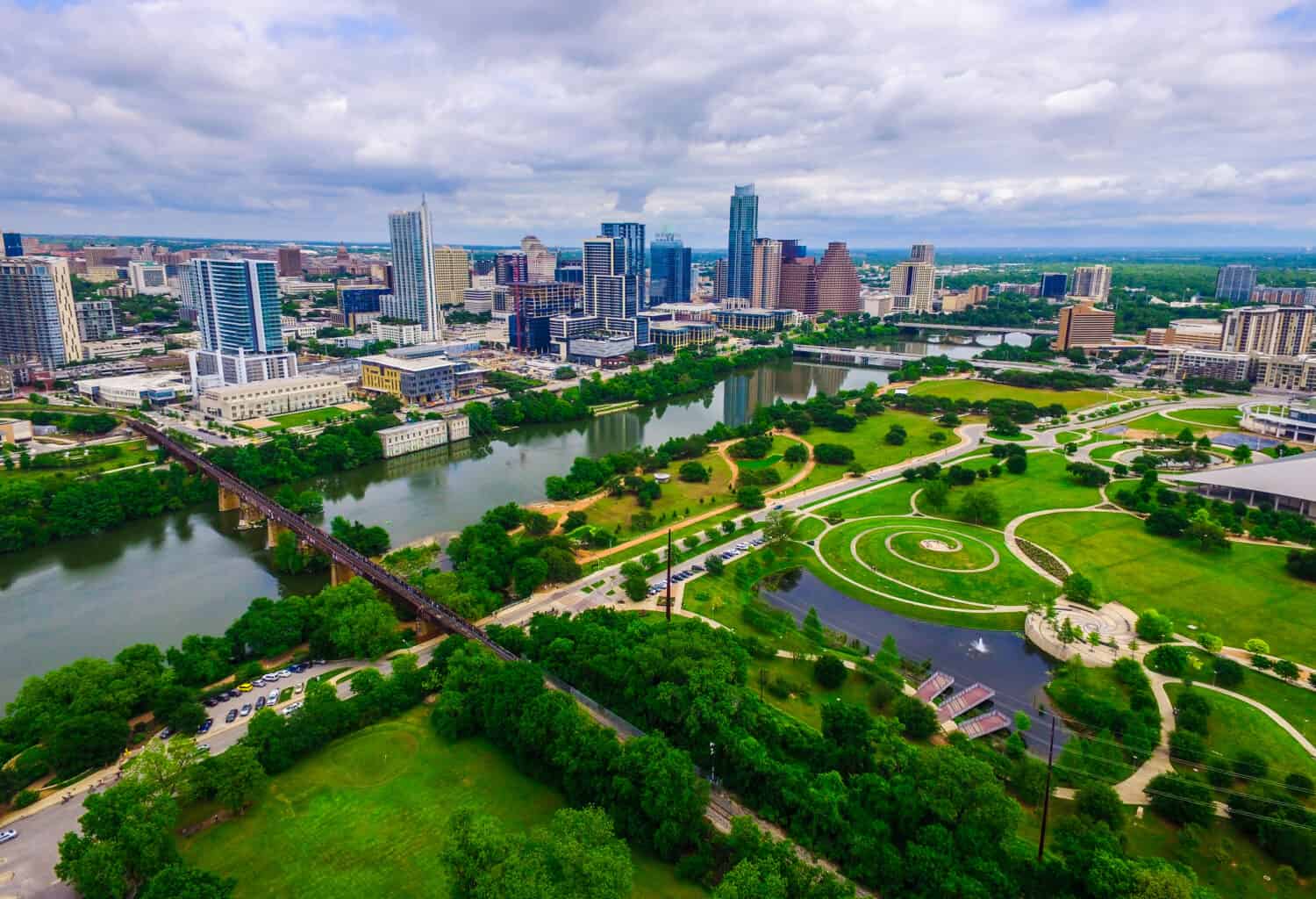 Aerial Over Austin Texas spring time colors with Railroad Tracks crossing Lady bird lake at Zilker Park and Auditorium Shores with Skyline Cityscape and downtown in the background North of the River