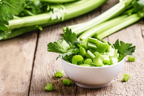 Fresh sliced celery in a white bowl on a vintage wooden background, selective focus