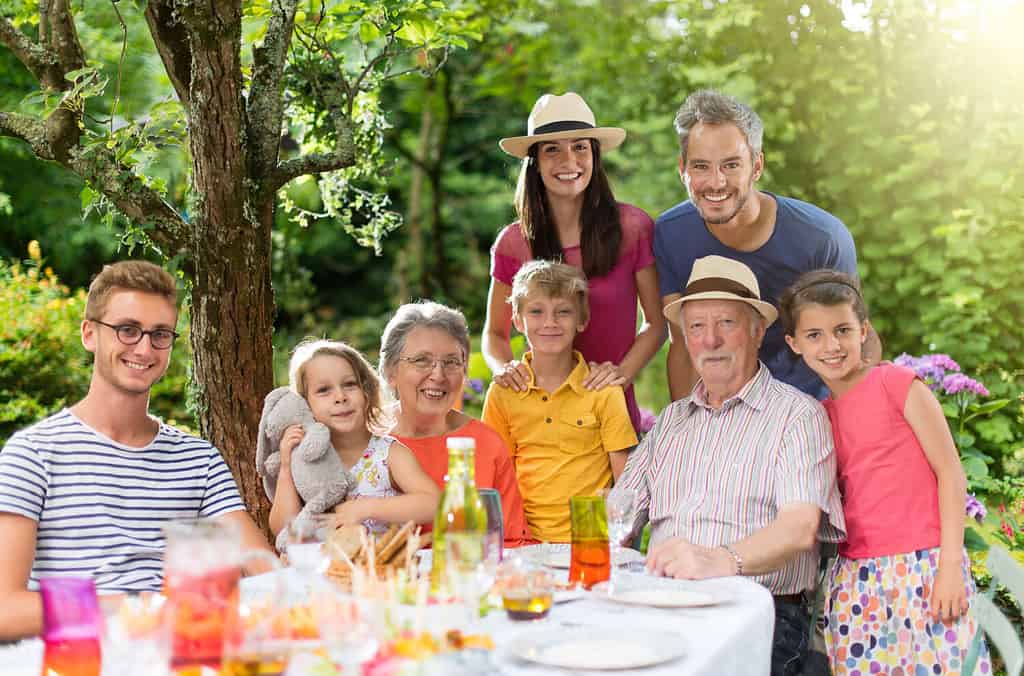 In summer, Family reunion around a picnic table in a beautiful garden. All generations pose for the camera. Shot with flare