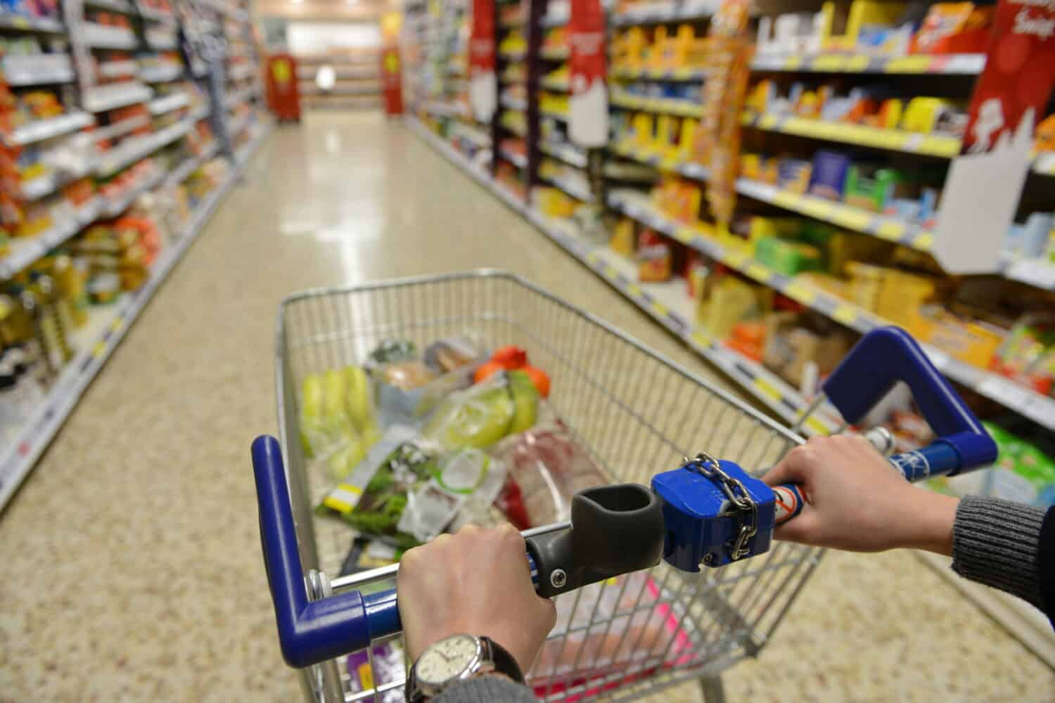 Shopper Pushes a Cart with Grocery Products in Supermarket Aisle - Image Has a Shallow Depth of Field