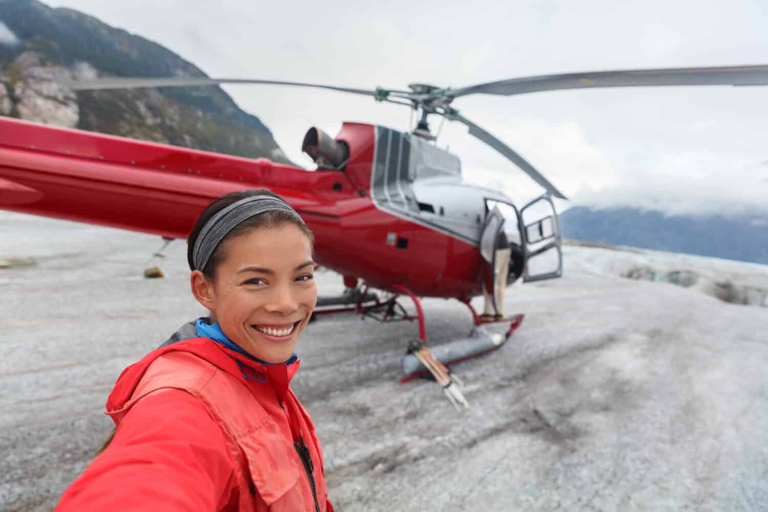 Happy tourist taking selfie picture on helicopter tour excursion. Asian woman cruise passenger on shore activity glacier walk hike in Alaska, USA.