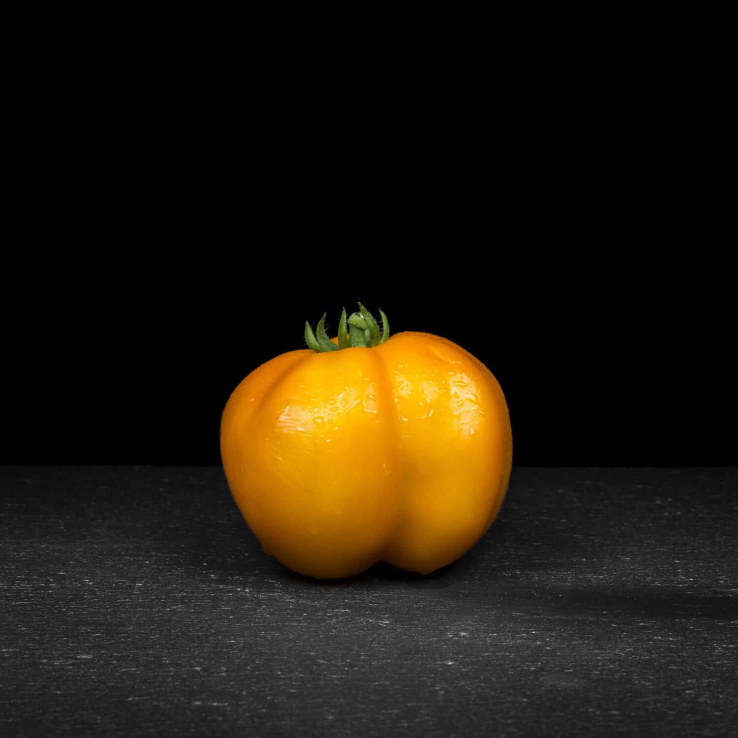 Tomato (breed: Yellow Stuffer) with water droplets on black slate with dark background (solanum lycopersicum)