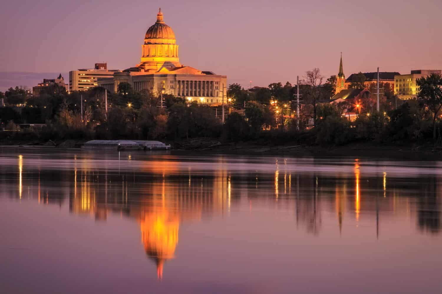 Cityscape of the Jefferson City skyline with the Missouri State Capitol reflecting in the river at twilight.