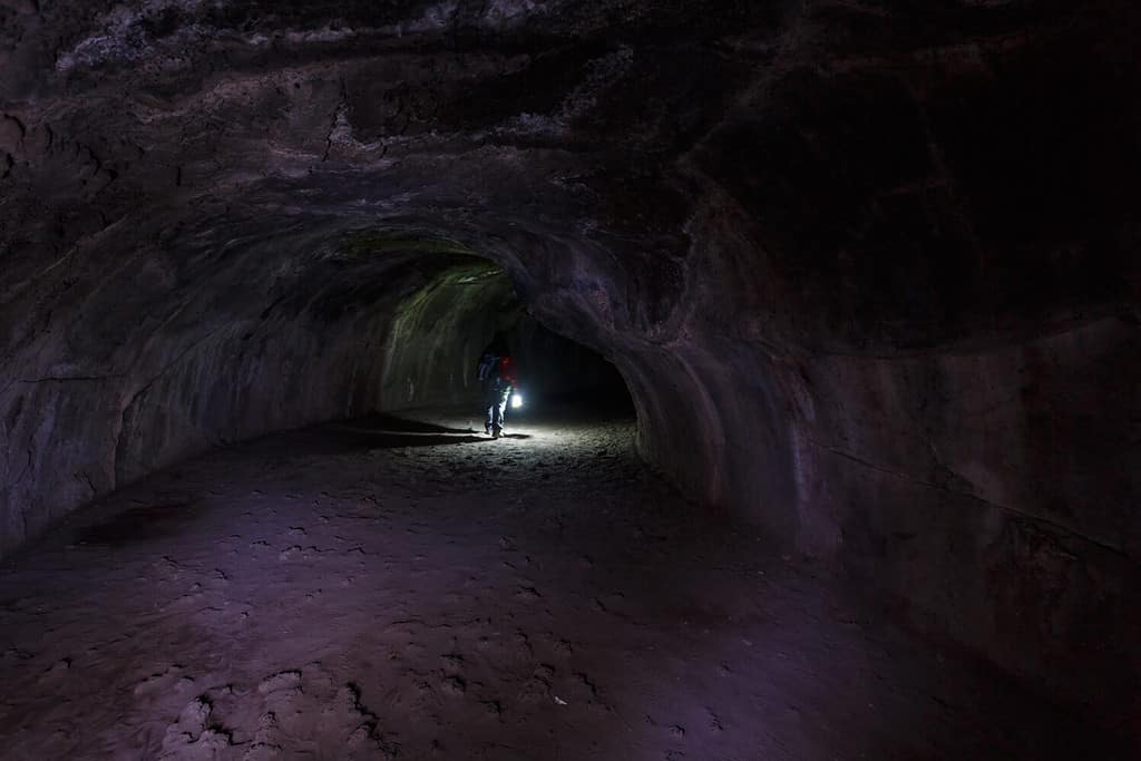 Hiker with lantern walks through Lassen Volcanic National Parks Lava tube a cave made during molten lava flow