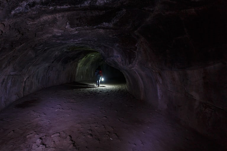 Hiker with lantern walks through Lassen Volcanic National Parks Lava tube a cave made during molten lava flow