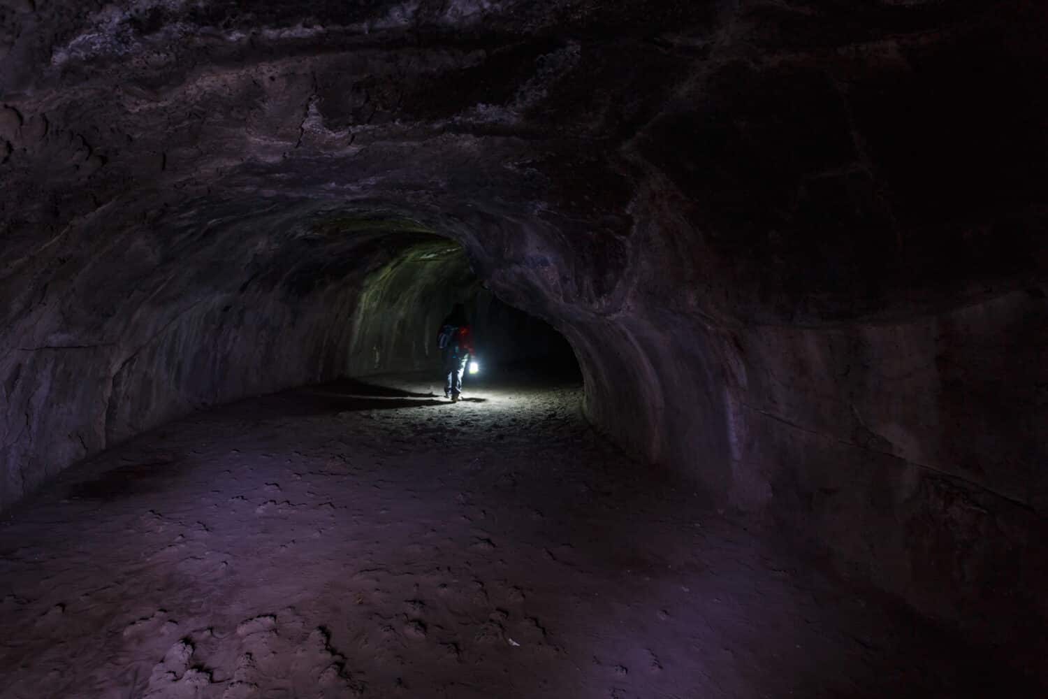 Hiker with lantern walks through Lassen Volcanic National Parks Lava tube a cave made during molten lava flow