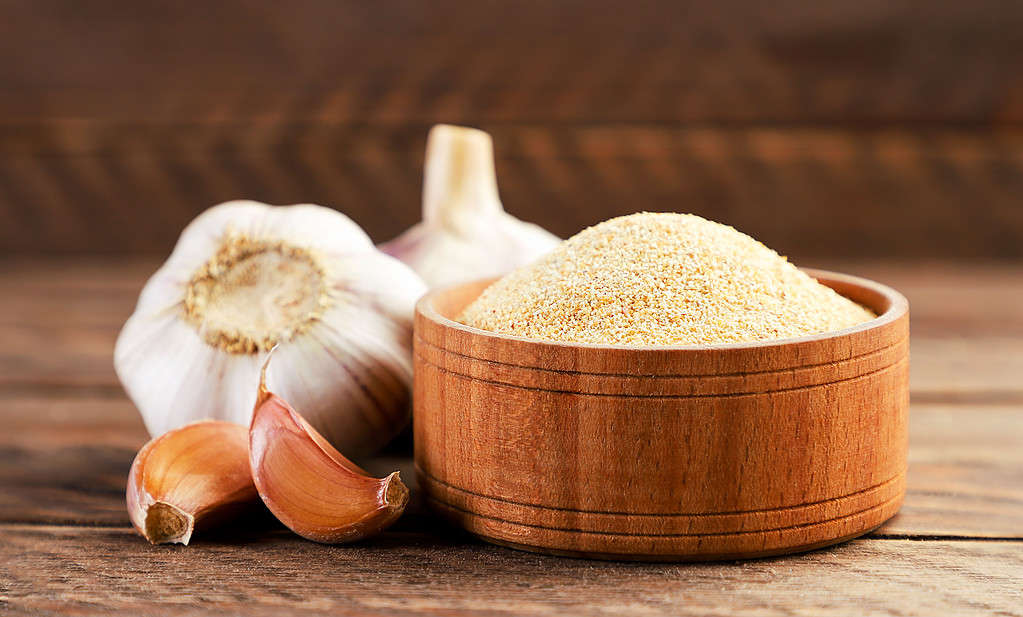 garlic powder Ground garlic in a plate and cloves on a wooden background