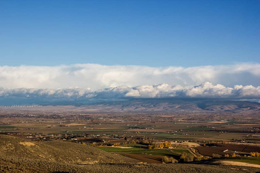 View of a valley and city with clouds and mountain range in the background.