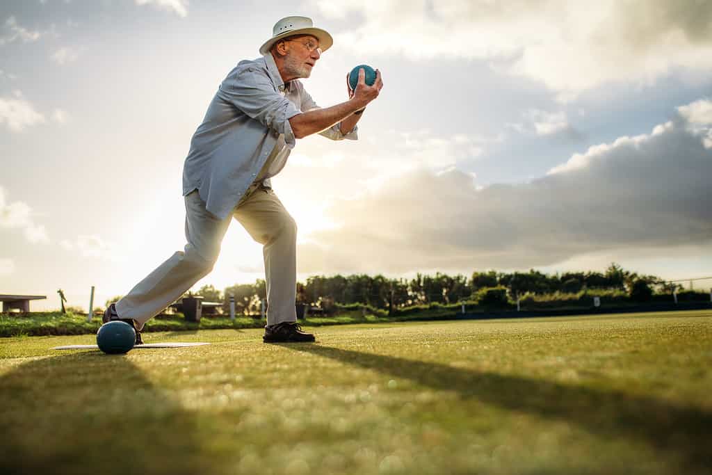 Man about to throw a bocce ball across a lawn field.