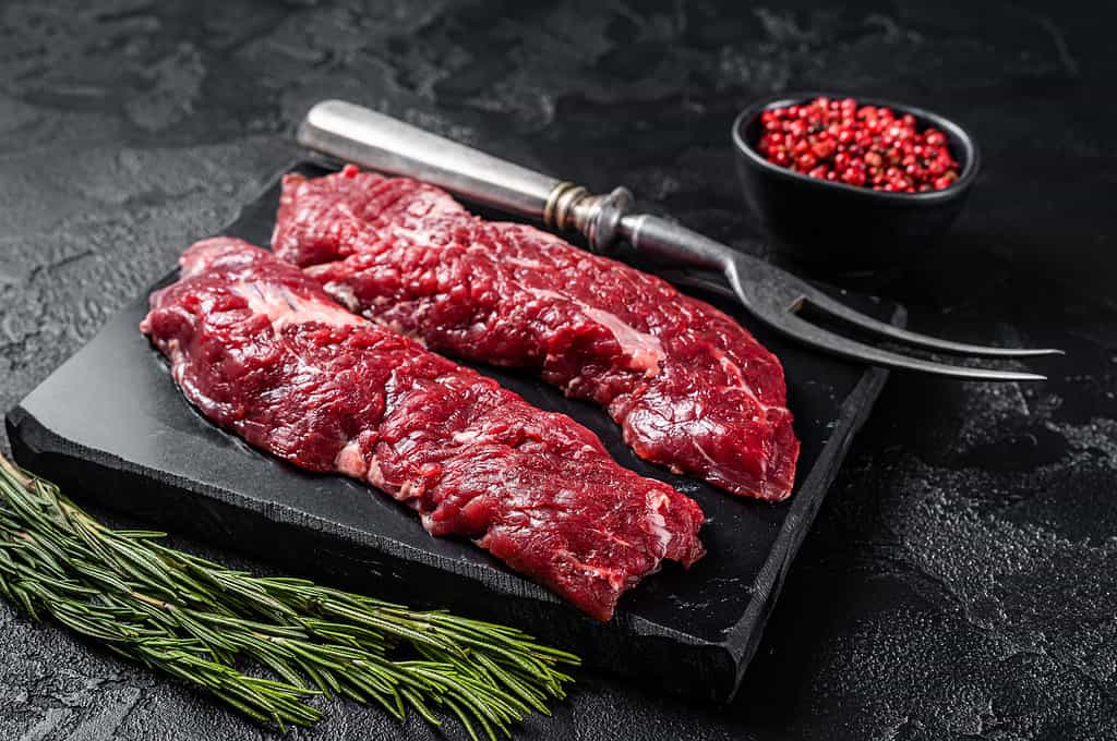 Raw Machete steak or hanging tender cut with herbs. Black background. Top view
