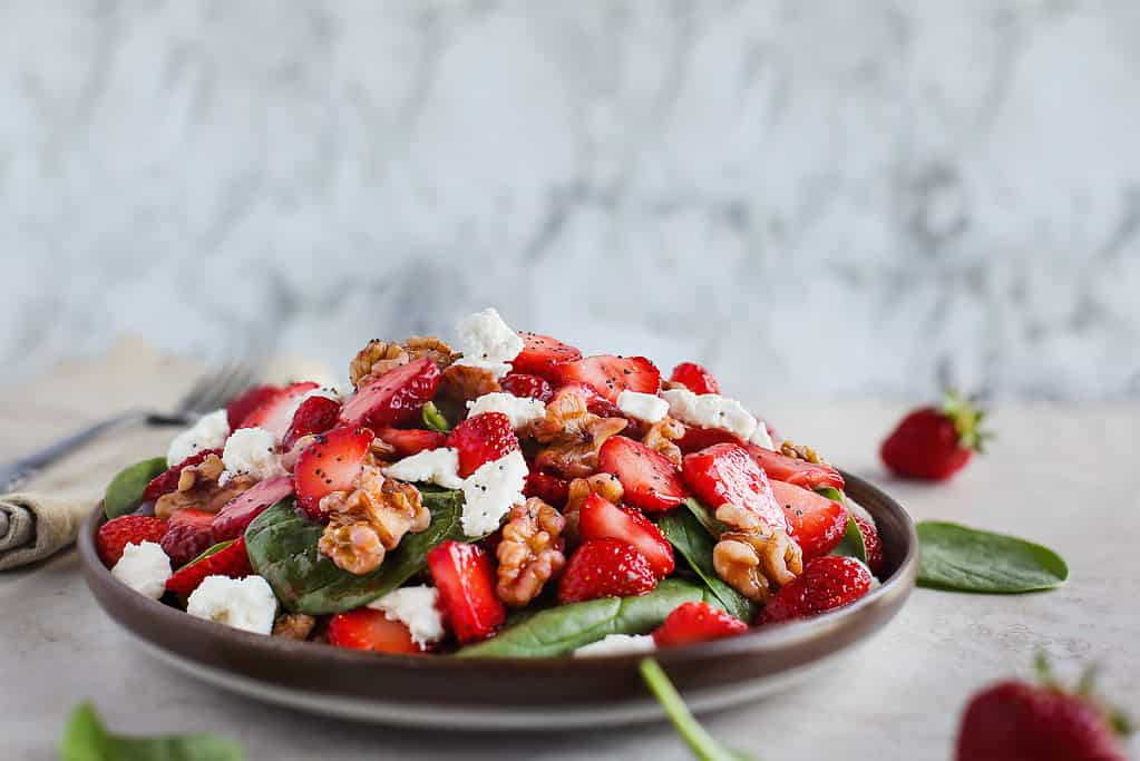 Plate of homemade fresh salad of baby spinach leaves, sliced strawberries, walnuts, feta cheese, and a light vinaigrette dressing.