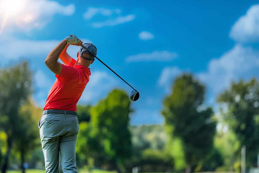 A man swings a golf course on a sunny day.