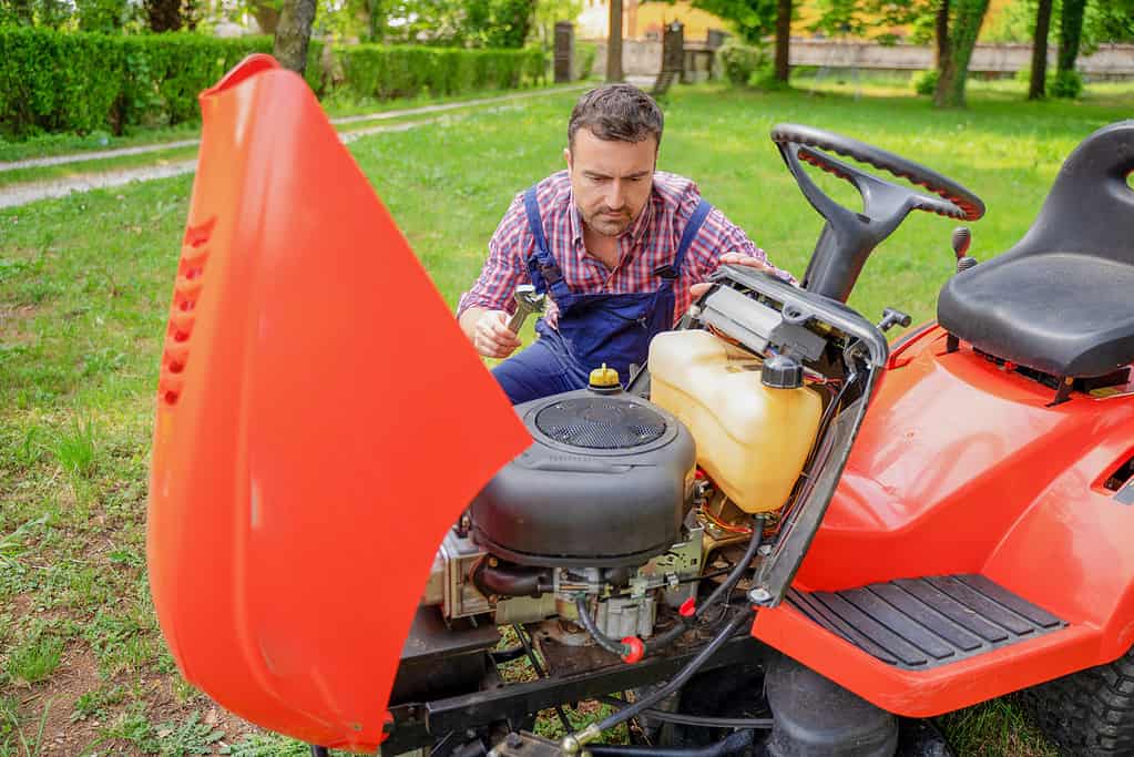 One gardener mowing grass fixing lawn mower engine problem