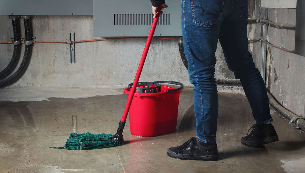 Woman mopping flood from water leaks in basement or electrical room.