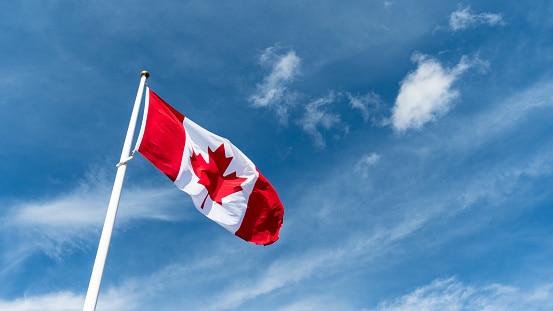 Canada Flag Pole Waving in the Wind Against Blue Sky Background
