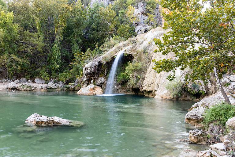 Water cascading over rocks into a natural pool at Turner Falls in Oklahoma, beautiful nature, water and rocks among trees.
