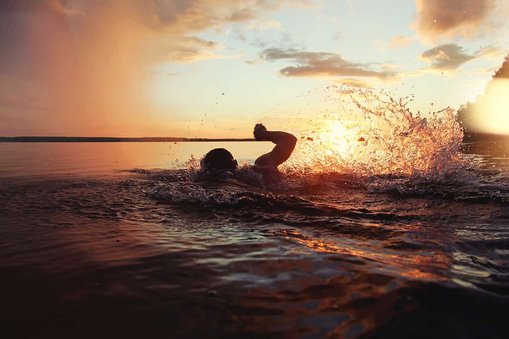 Athletic man is trained to swim in lake at sunset