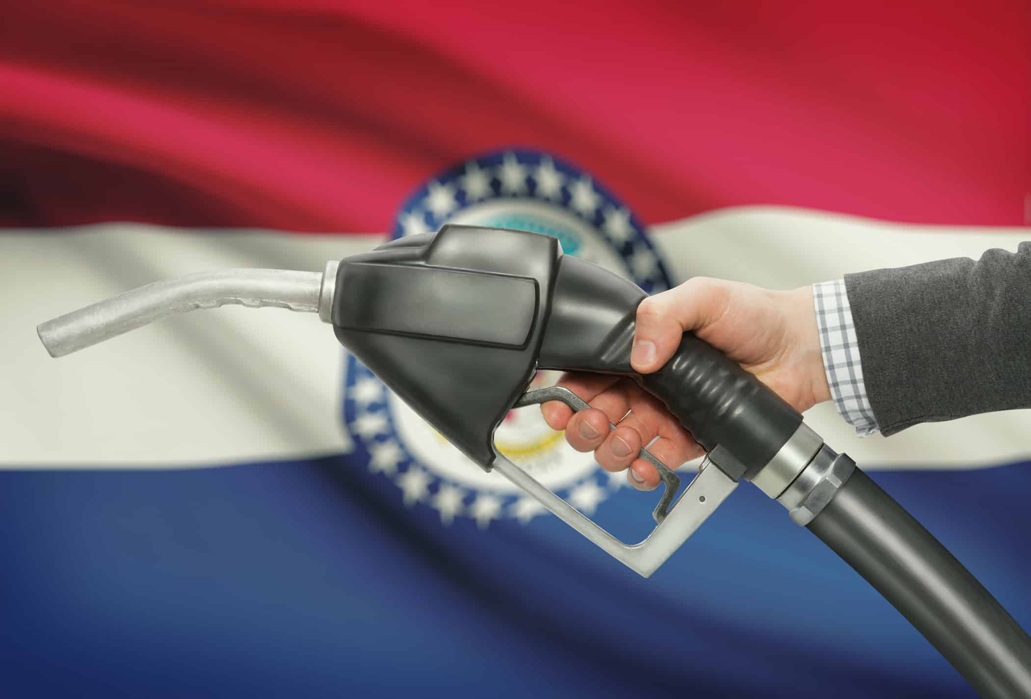 Fuel pump nozzle in hand with USA states flags on background - Missouri