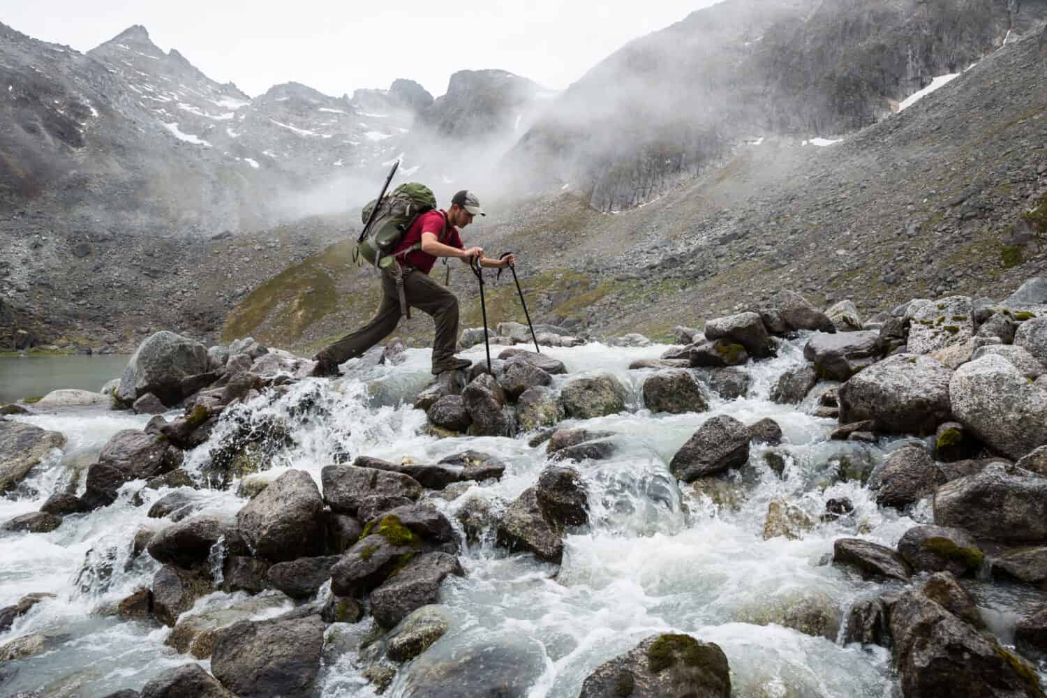 A man steps his way across a rocky river in the Talkeetna wilderness of Alaska
