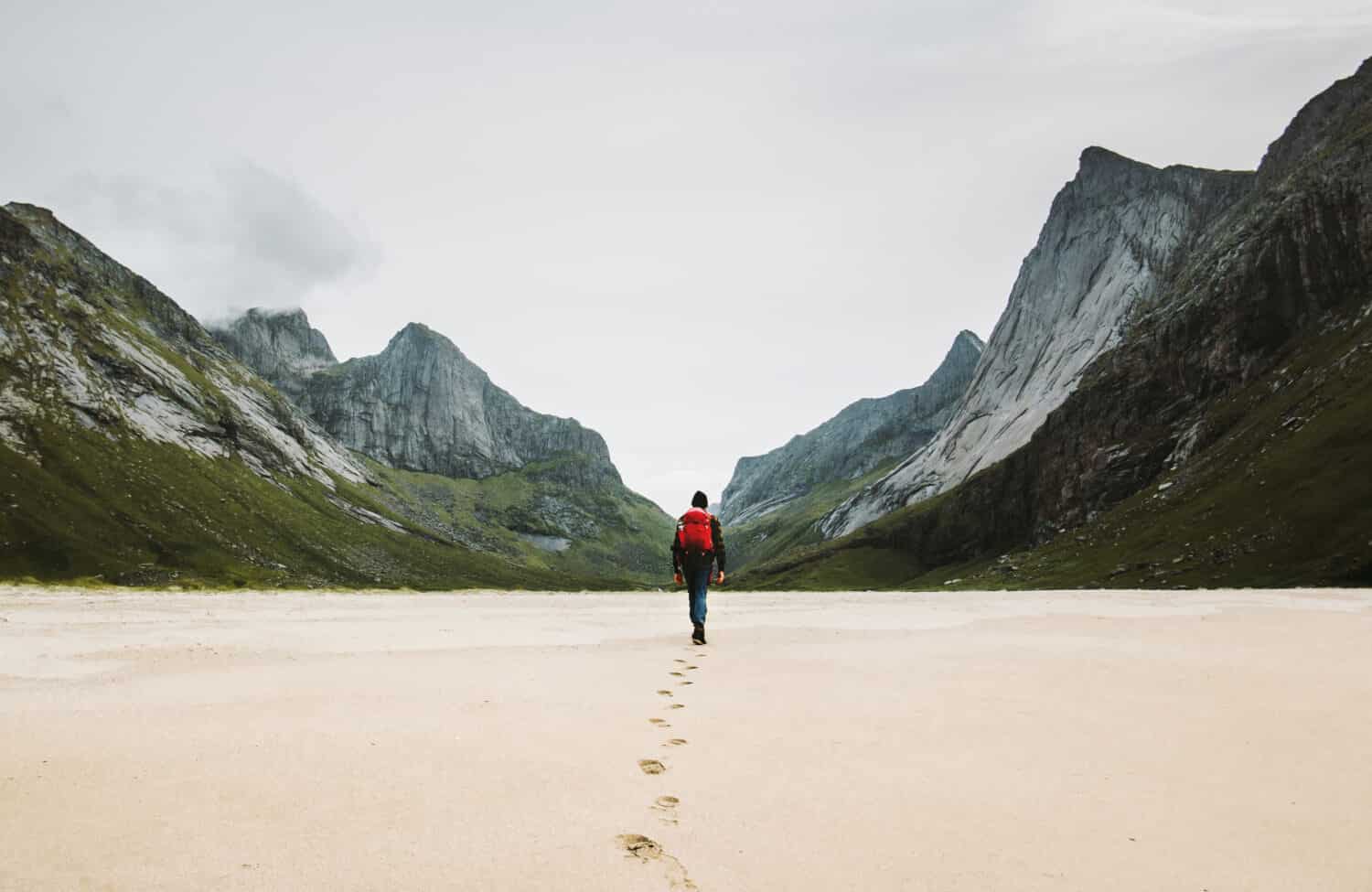 Man with backpack walking away alone at sandy beach in mountains Travel lifestyle concept adventure outdoor summer vacations in Norway wild nature 