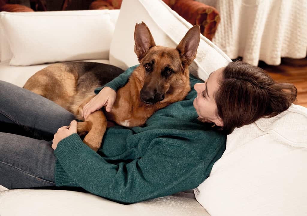 Beautiful portrait of smiling woman hugging her dog german shepherd together in front of fireplace at cozy home in winter day in happiness Friendship Love Companionship and benefits of pets animals.