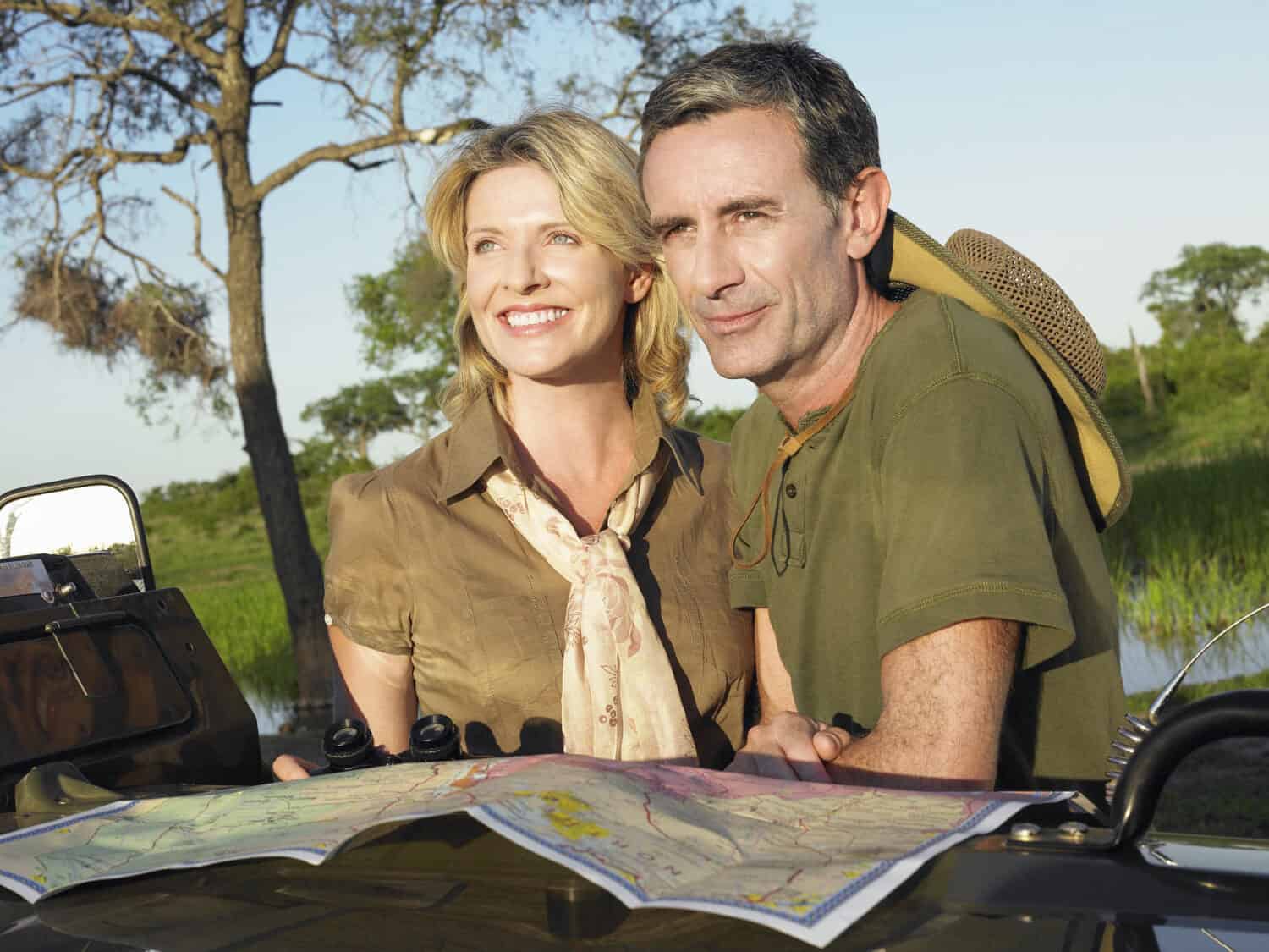 Smiling couple with at map on bonnet of jeep looking at view