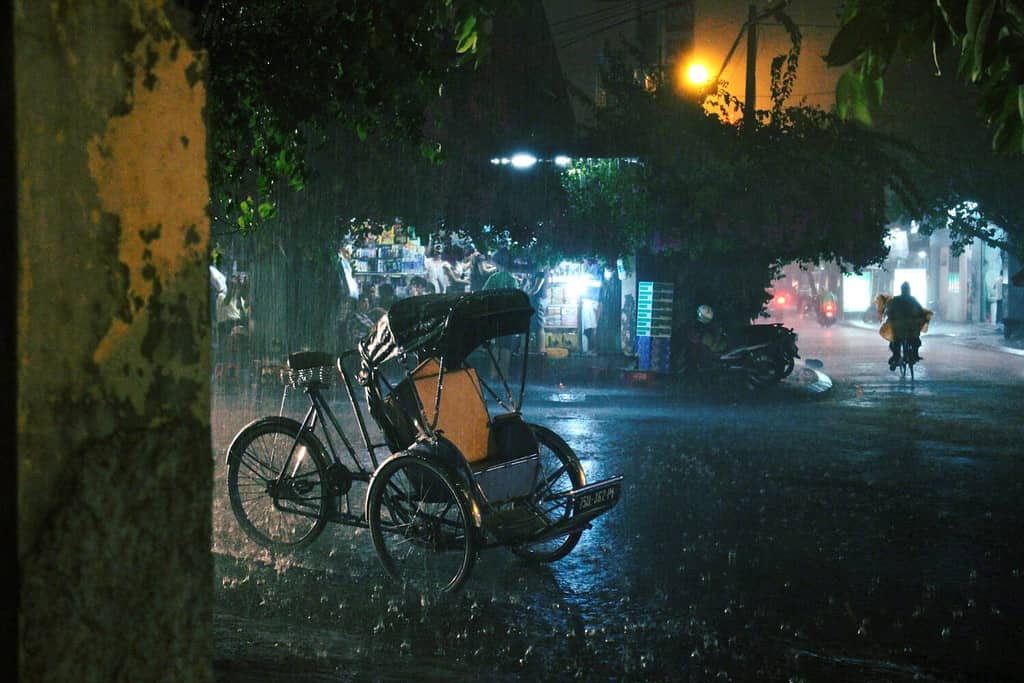 A cyclo (bicycle rickshaw) parked on the street during an evening downpour of rain, Hanoi, Vietnam.